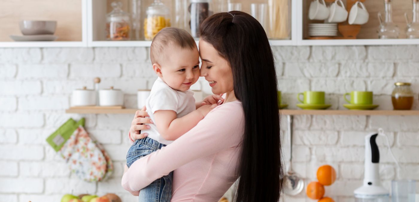 Mother smiling and holding her baby in a bright kitchen