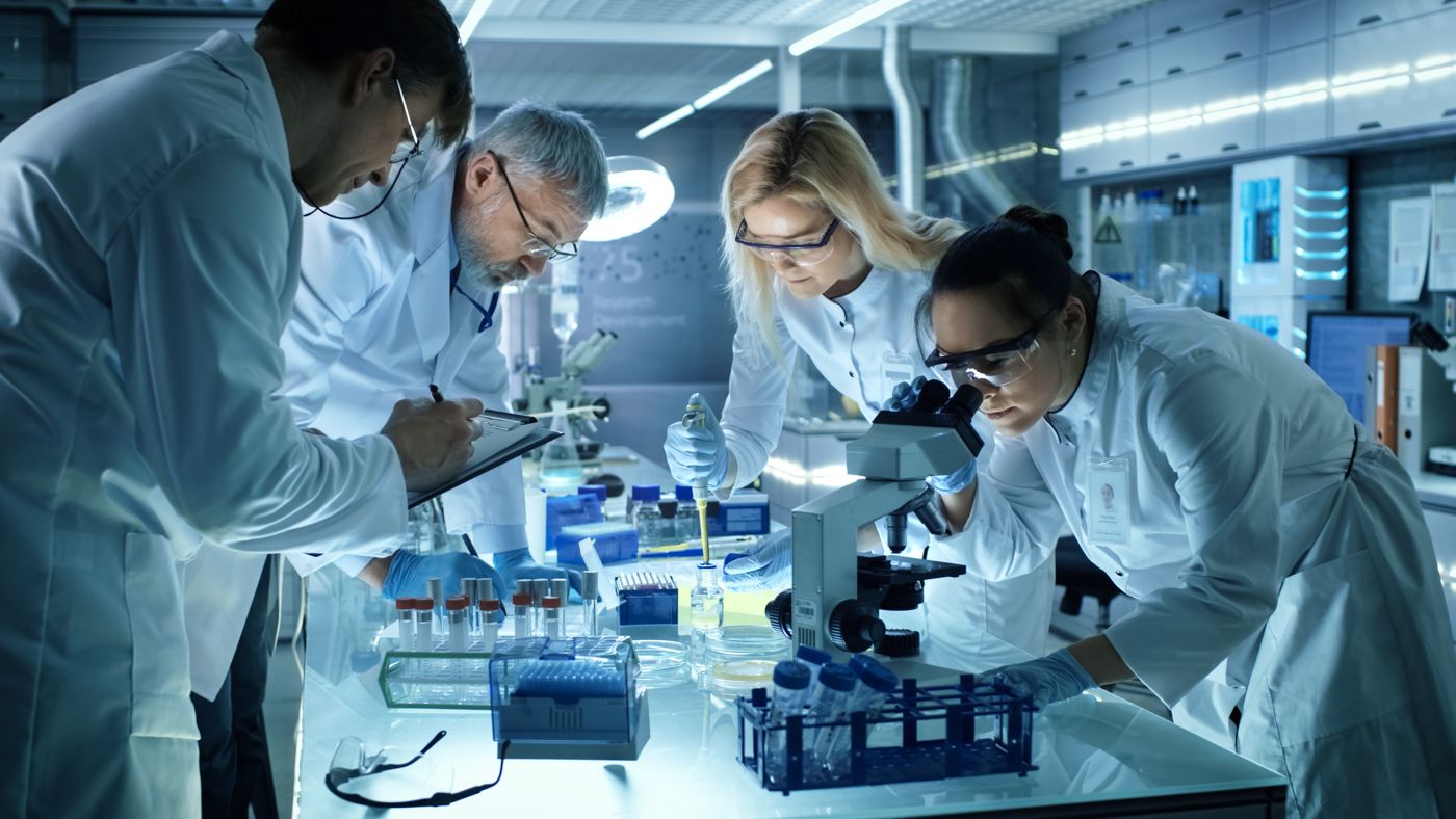 Laboratory scientists working together at a bench with a microscope and sample tubes